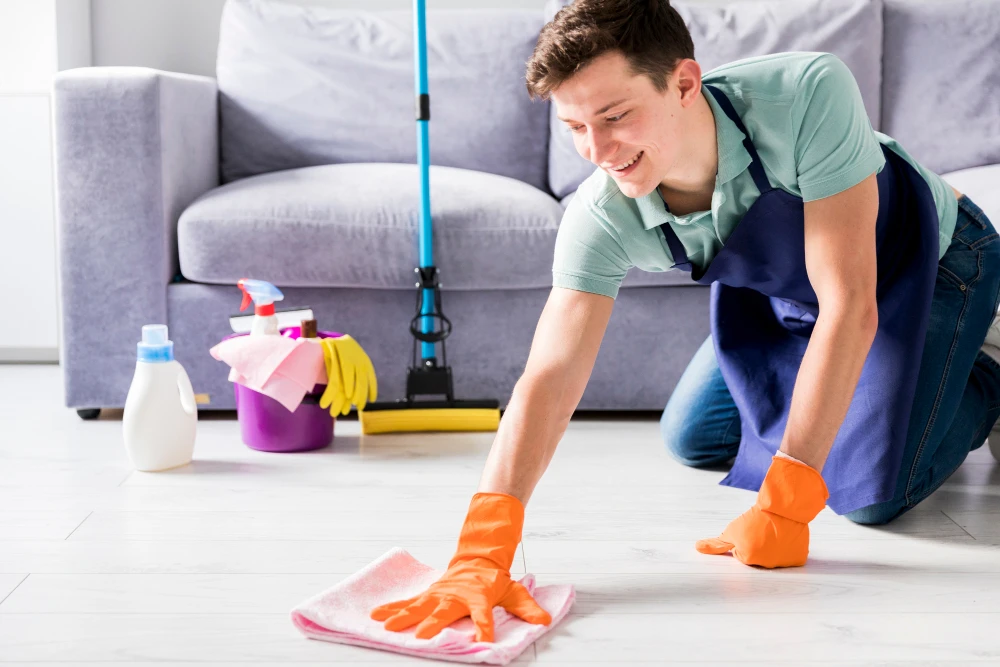 Cleaner hand-wiping a spill from a hard floor with a microfiber cloth.