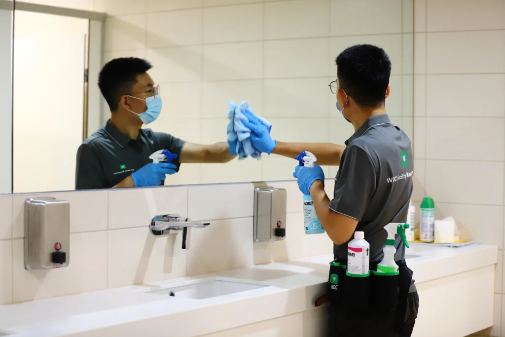 Two cleaners wiping and polishing a large restroom mirror for a streak-free finish.