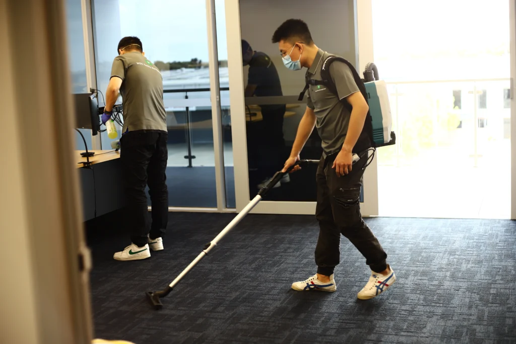 Janitor using an ergonomic backpack vacuum to clean carpets in a corporate workspace.