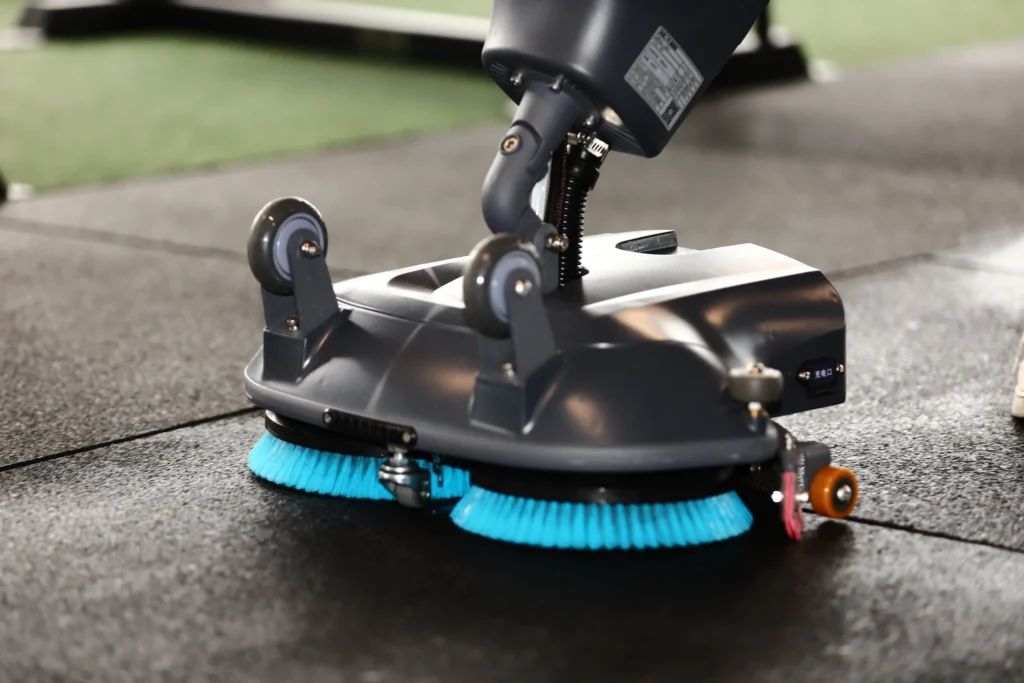 Close-up of industrial floor scrubber brushes cleaning a rubber gym floor.