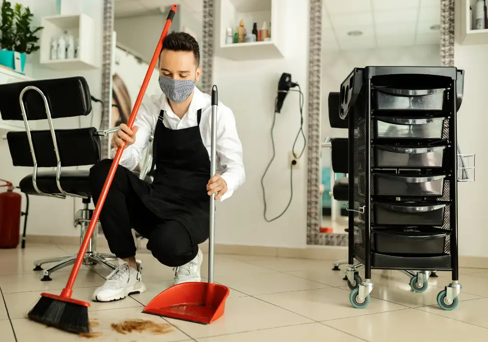 Janitor sweeping dust and debris from a commercial shop floor using a broom.