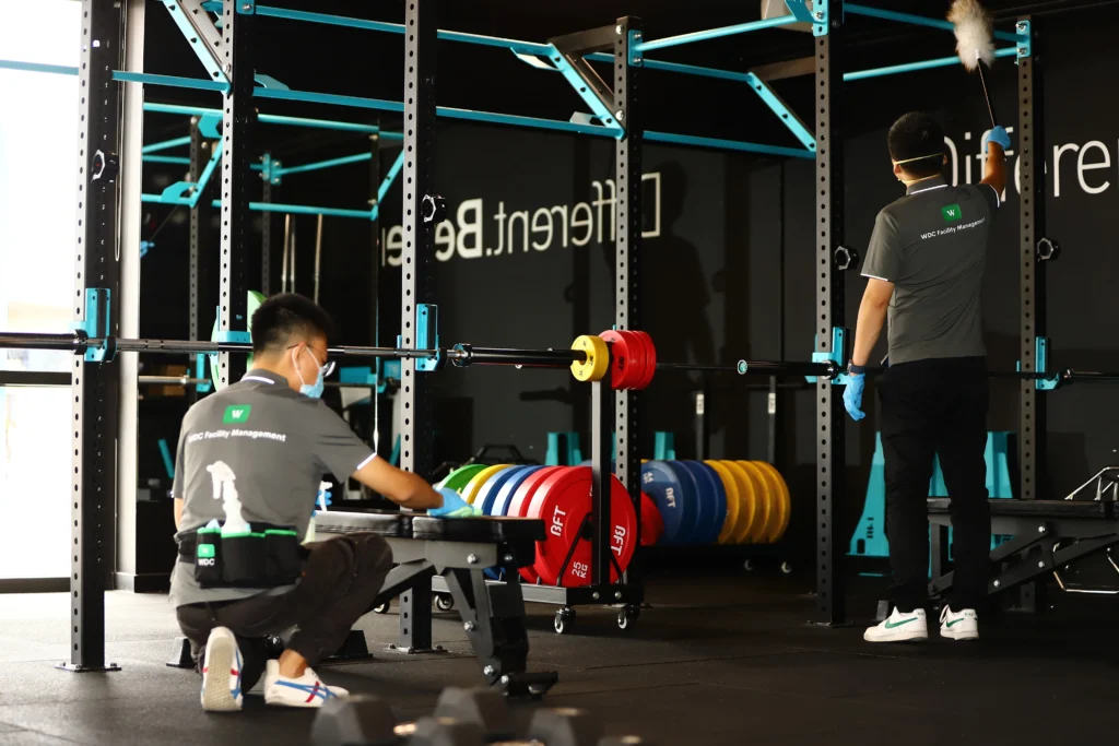 Cleaning staff sanitizing gym weights and racks to prevent cross-contamination.
