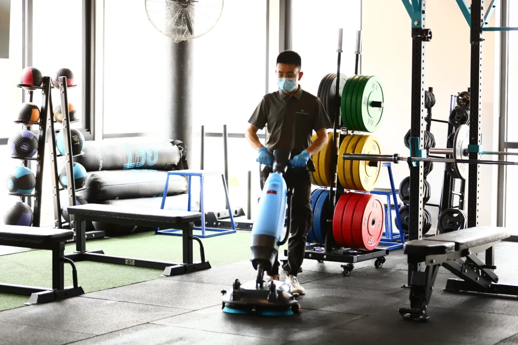 Industrial floor scrubber machine cleaning rubber flooring in a commercial gym.