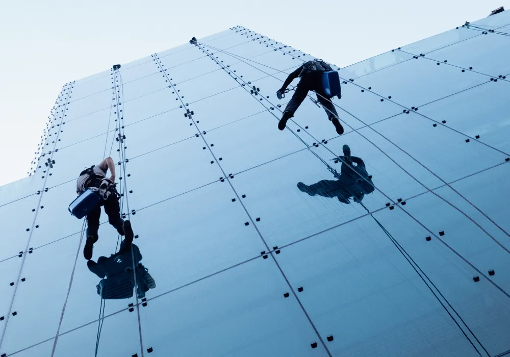 Rope access technicians abseiling to clean windows on a high-rise glass skyscraper.