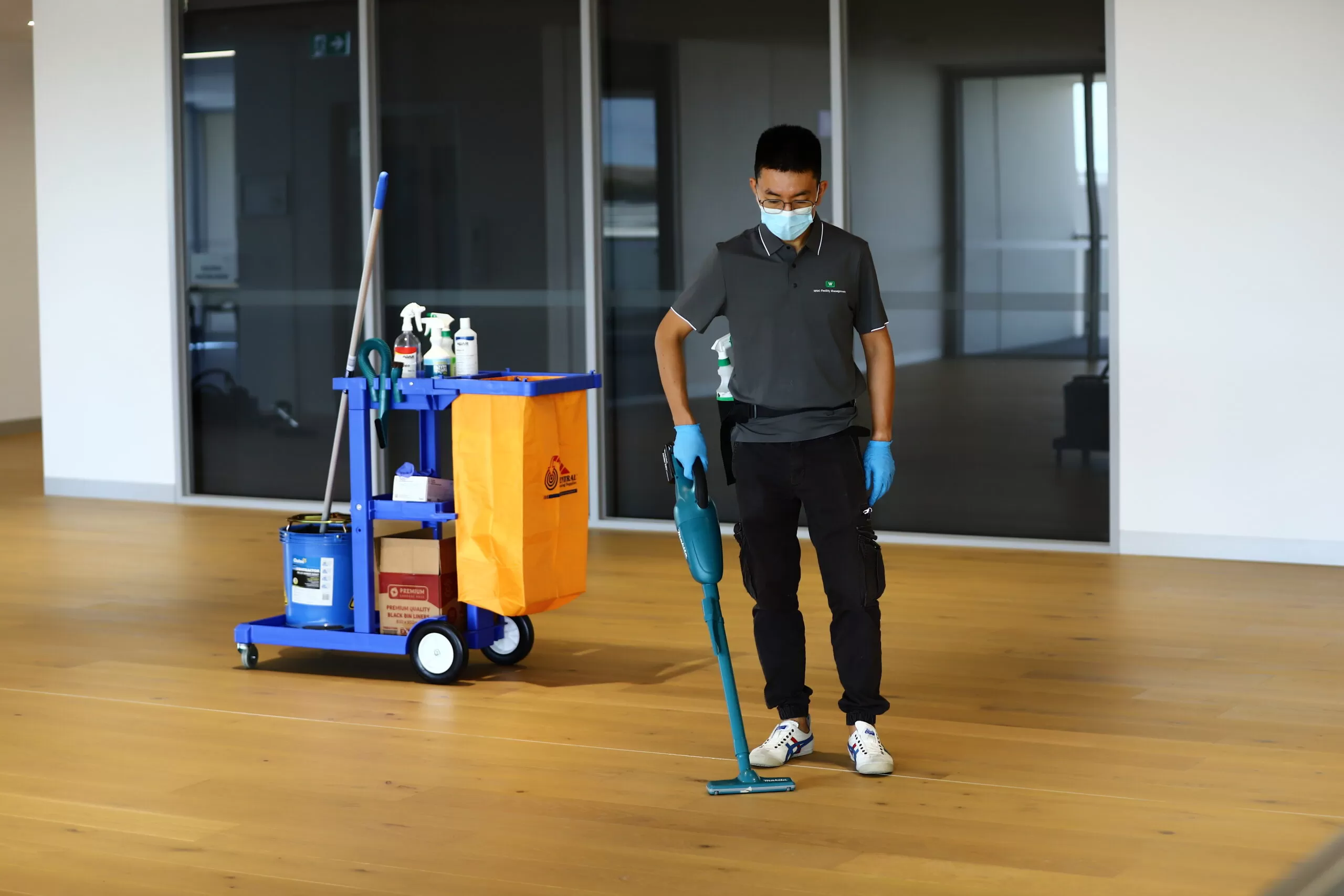Janitor with a yellow mop bucket standing in a polished office corridor.