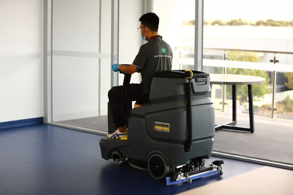 Professional cleaner operating a ride-on floor scrubber in a spacious commercial facility.