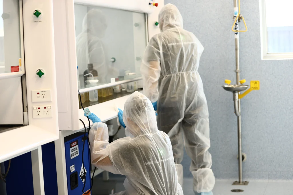 Disinfection team sanitizing high-tech laboratory workstations in protective gear.