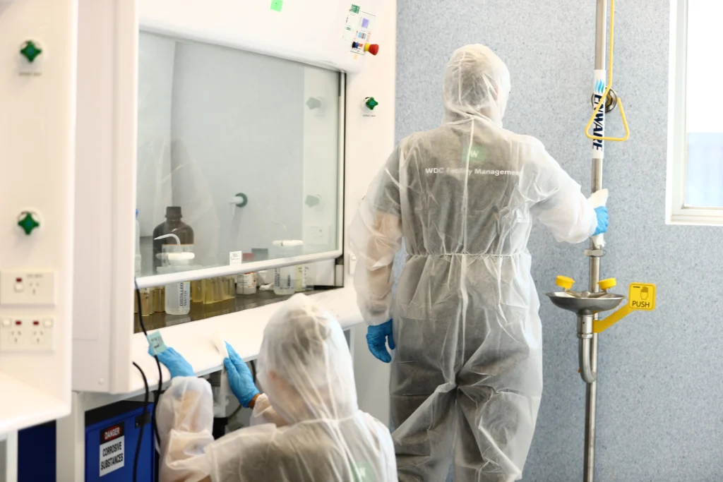 Team in hazmat suits performing biohazard cleaning in a laboratory setting.