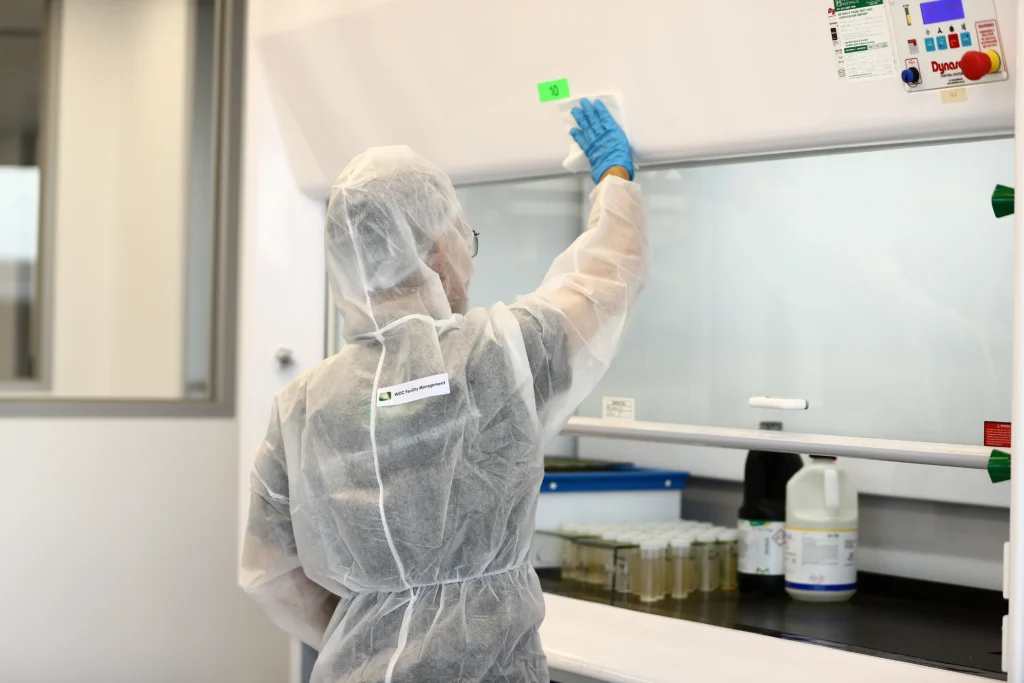 Specialist cleaner in full white PPE suit disinfecting a cleanroom glass window.