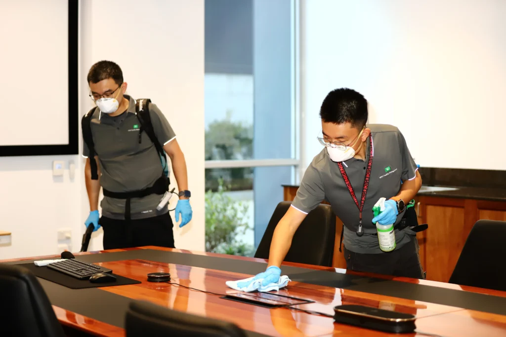 Cleaner wiping and polishing a large wooden boardroom table for a corporate client.