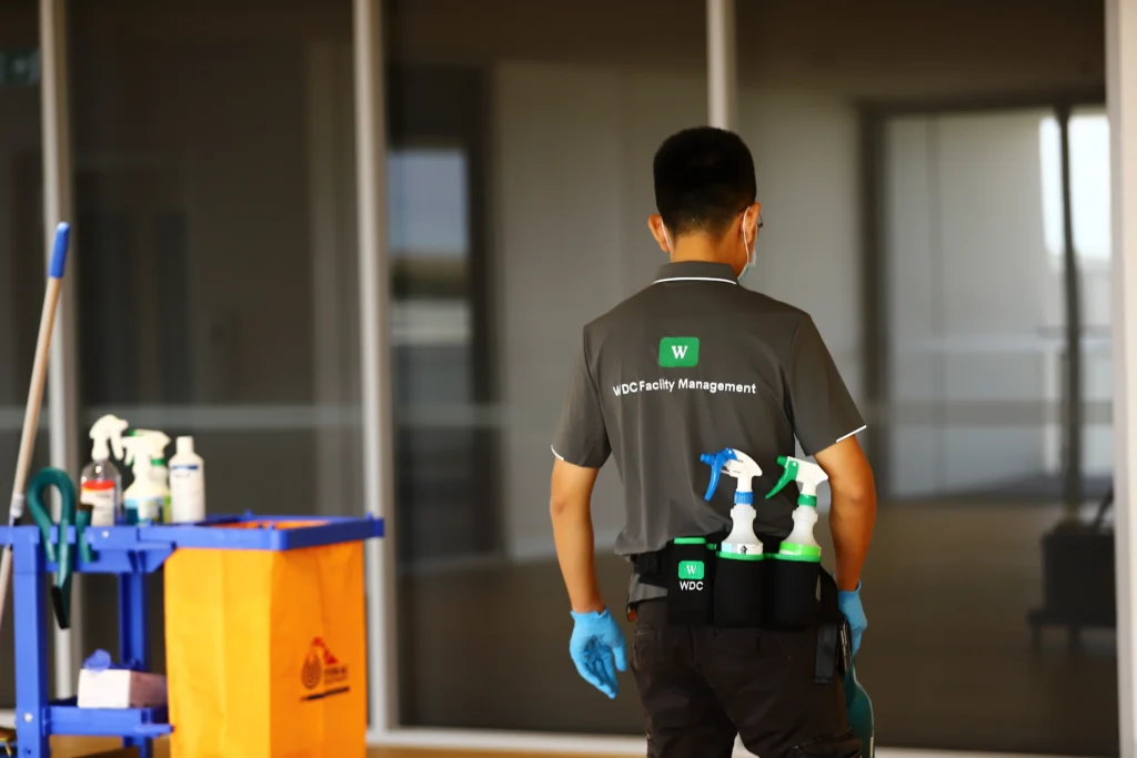 Rear view of janitorial staff wearing a utility belt with cleaning supplies.