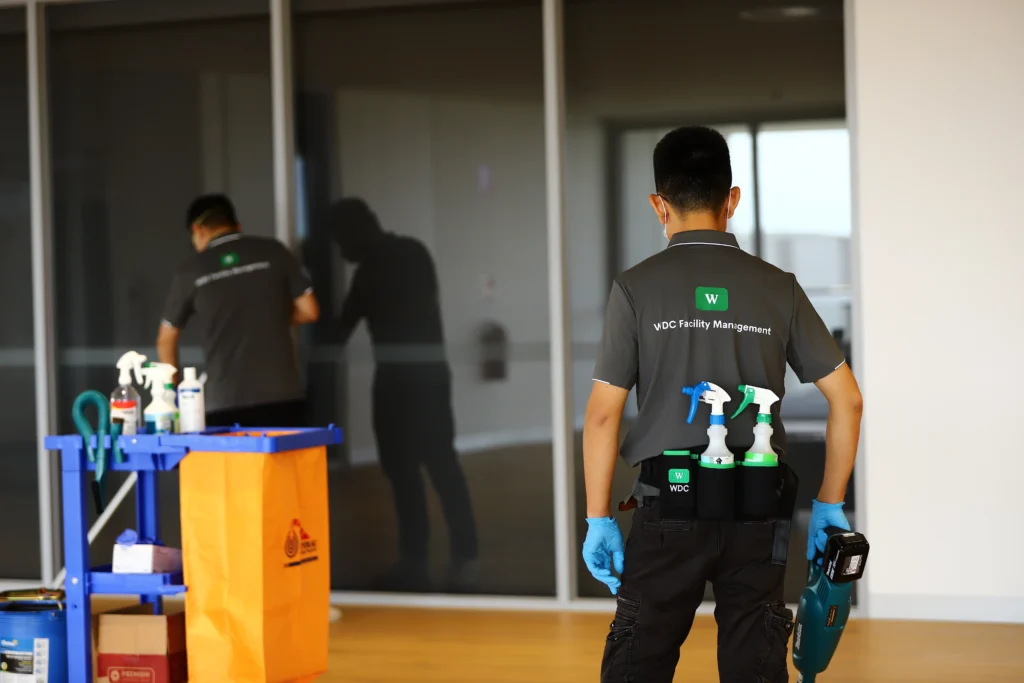 Commercial cleaner with spray bottles patrolling an office glass corridor.